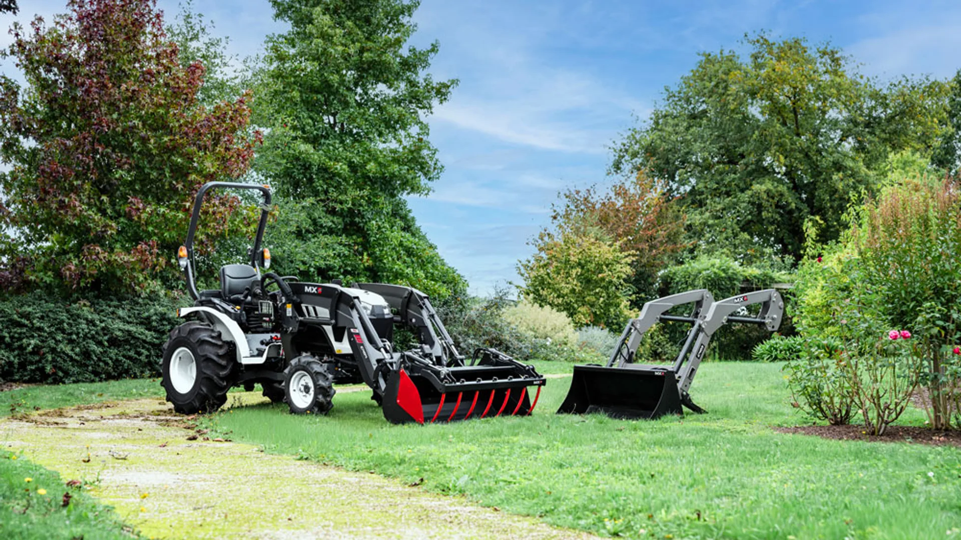 Tractor compact cu încărcător frontal și cupă pe un gazon, lângă un atașament de încărcare.