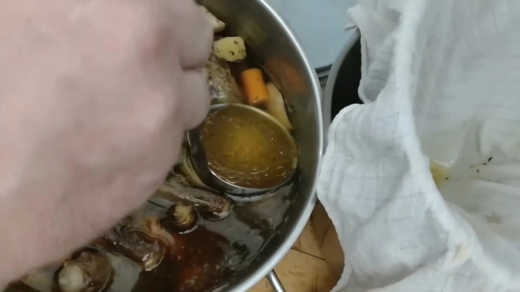 Polonic cu supă limpede deasupra oaselor și legumelor fierte în oală